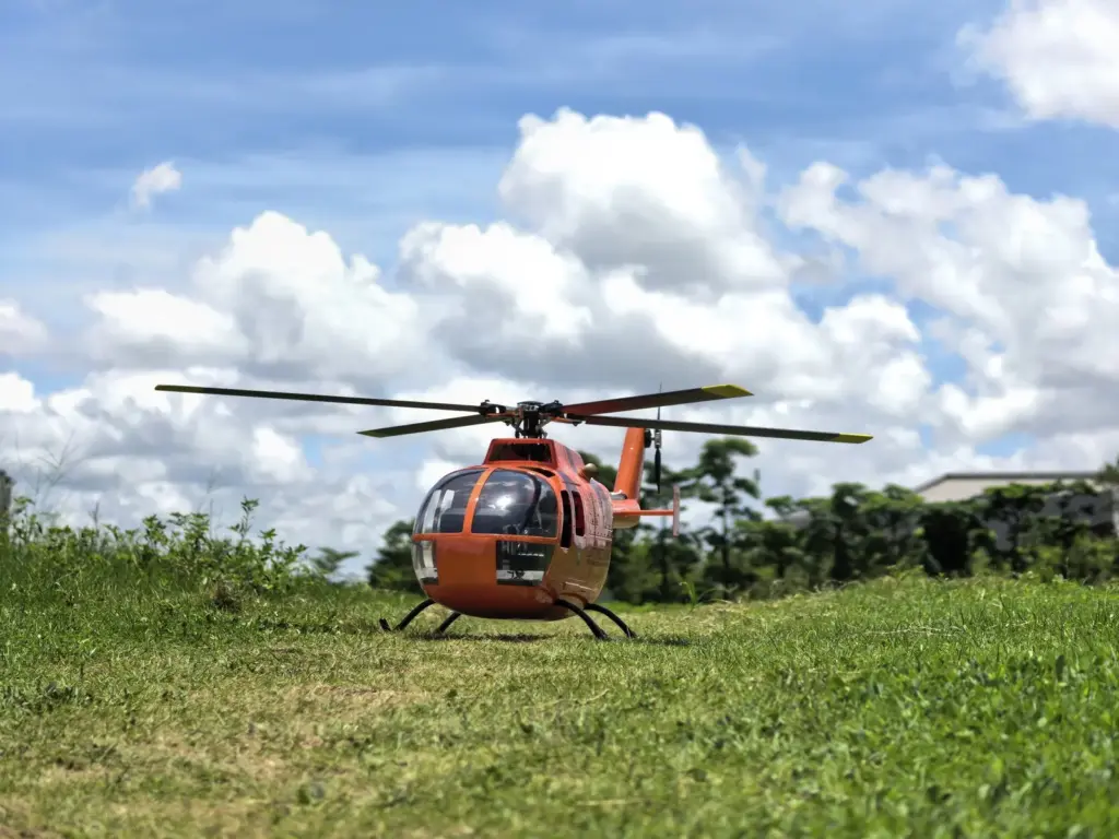 FLISHRC BO105 orange scale RC helicopter on grass under a cloudy sky